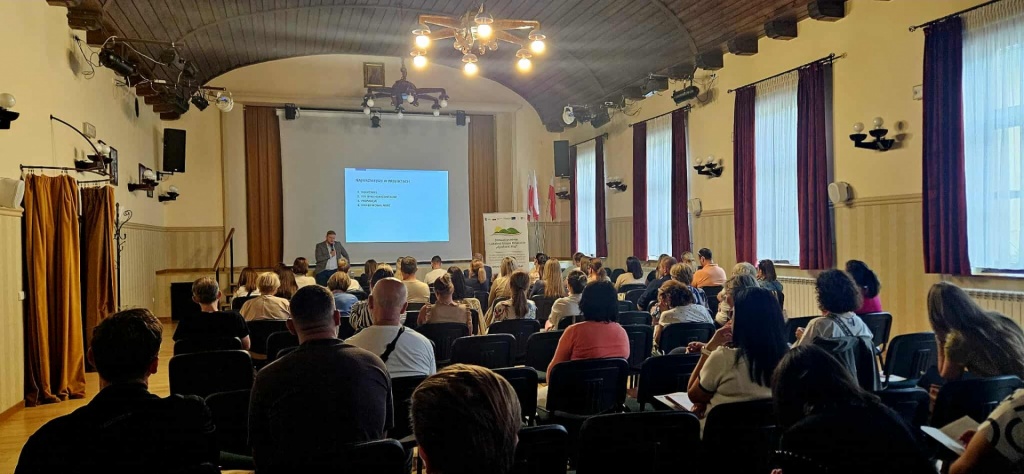 Widok og&oacute;lny sali konferencyjnej z&nbsp;uczestnikami szkolenia siedzącymi w&nbsp;rzędach i&nbsp;słuchającymi prelekcji. W&nbsp;tle widoczny baner LGD oraz okna z&nbsp;zasłonami.