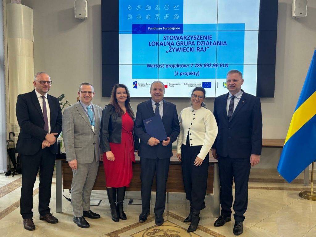 „Zdjęcia dokumentujące uroczyste wręczenie Listów Gratulacyjnych w dniu 31 marca 2026 r. w Urzędzie Marszałkowskim w Katowicach. Na fotografiach przedstawiono przedstawicieli Stowarzyszenia – Lokalnej Grupy Działania „Żywiecki Raj” oraz uczestników wydarzenia podczas wystąpienia, wręczenia dokumentów i wspólnego zdjęcia. W tle widoczny ekran prezentacyjny z informacją o projektach oraz flagi Polski i Unii Europejskiej.”