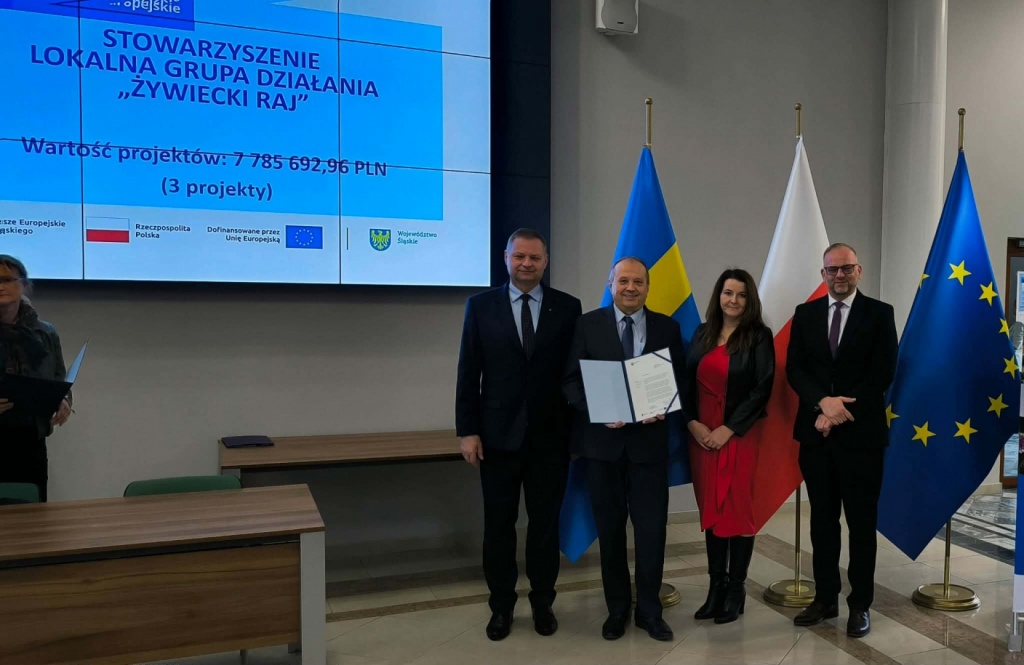 „Zdjęcia dokumentujące uroczyste wręczenie Listów Gratulacyjnych w dniu 31 marca 2026 r. w Urzędzie Marszałkowskim w Katowicach. Na fotografiach przedstawiono przedstawicieli Stowarzyszenia – Lokalnej Grupy Działania „Żywiecki Raj” oraz uczestników wydarzenia podczas wystąpienia, wręczenia dokumentów i wspólnego zdjęcia. W tle widoczny ekran prezentacyjny z informacją o projektach oraz flagi Polski i Unii Europejskiej.”